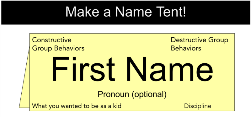 A photo of a name tent - a folded thick cardstock paper. Center says name with pronouns optional, each corner has an example are for additional quesitons